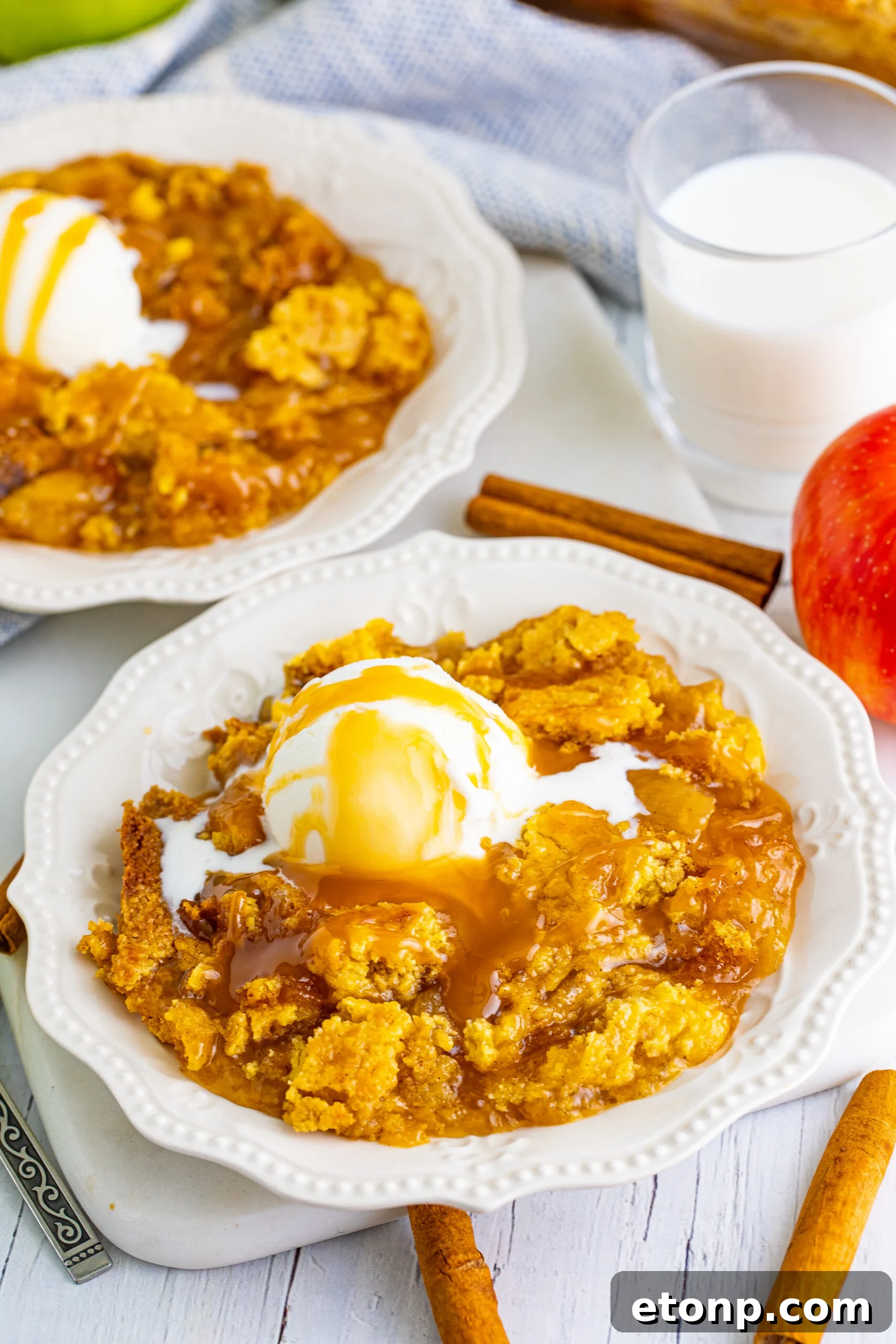 Close up shot of caramel apple dump cake topped with vanilla ice cream and caramel sauce.
