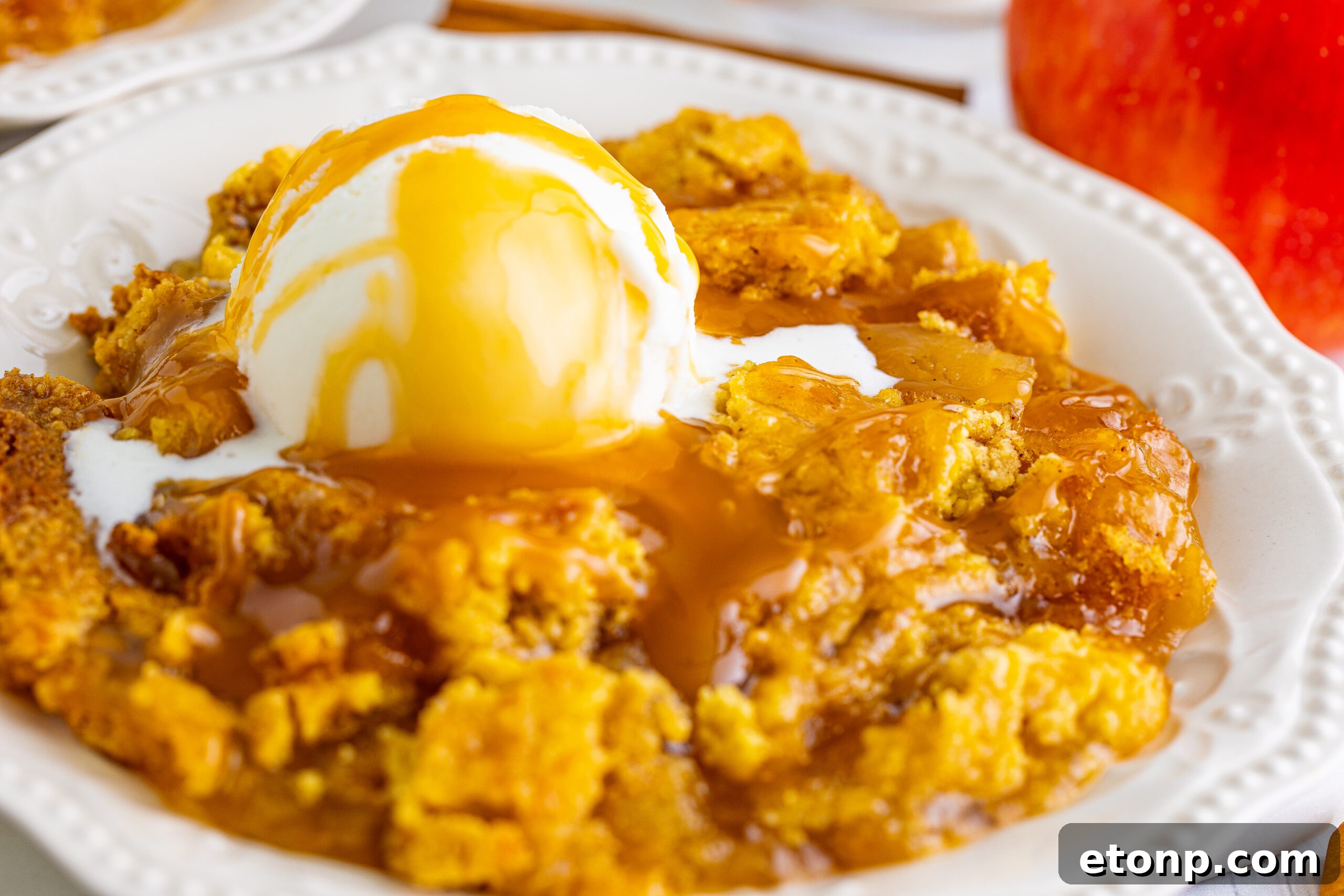 Close up shot of caramel apple dump cake topped with vanilla ice cream and caramel sauce.