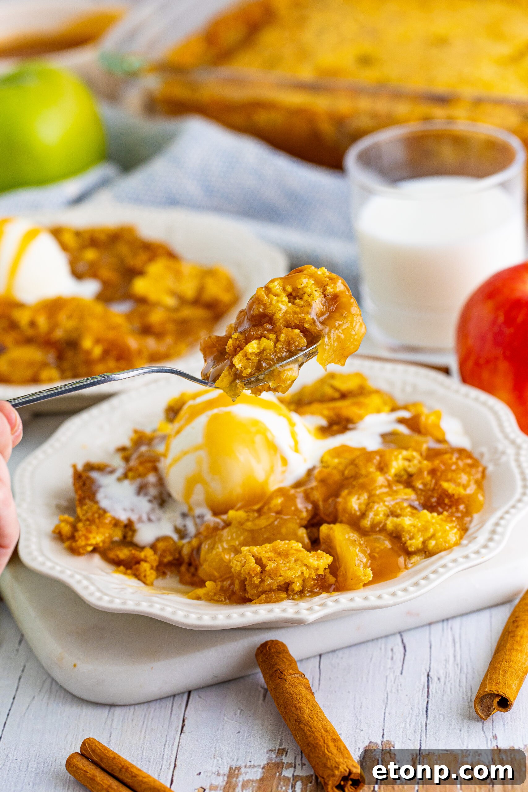 Close up shot of a spoon removing a bite of caramel apple dump cake from a white plate.