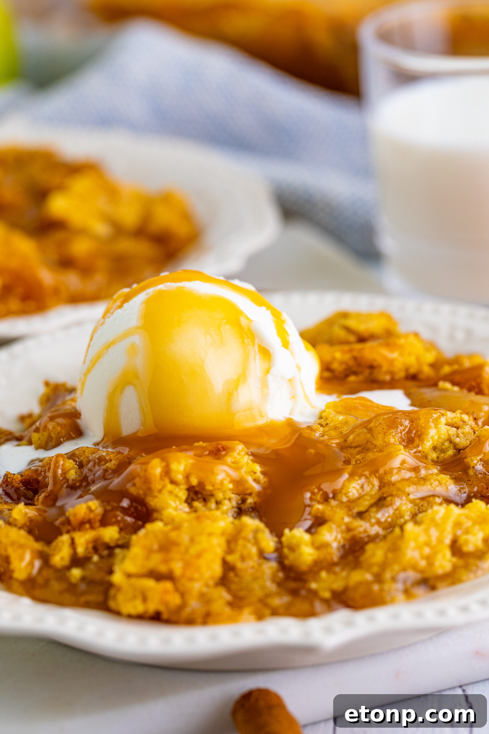 Close up shot of caramel apple dump cake topped with vanilla ice cream and caramel sauce.