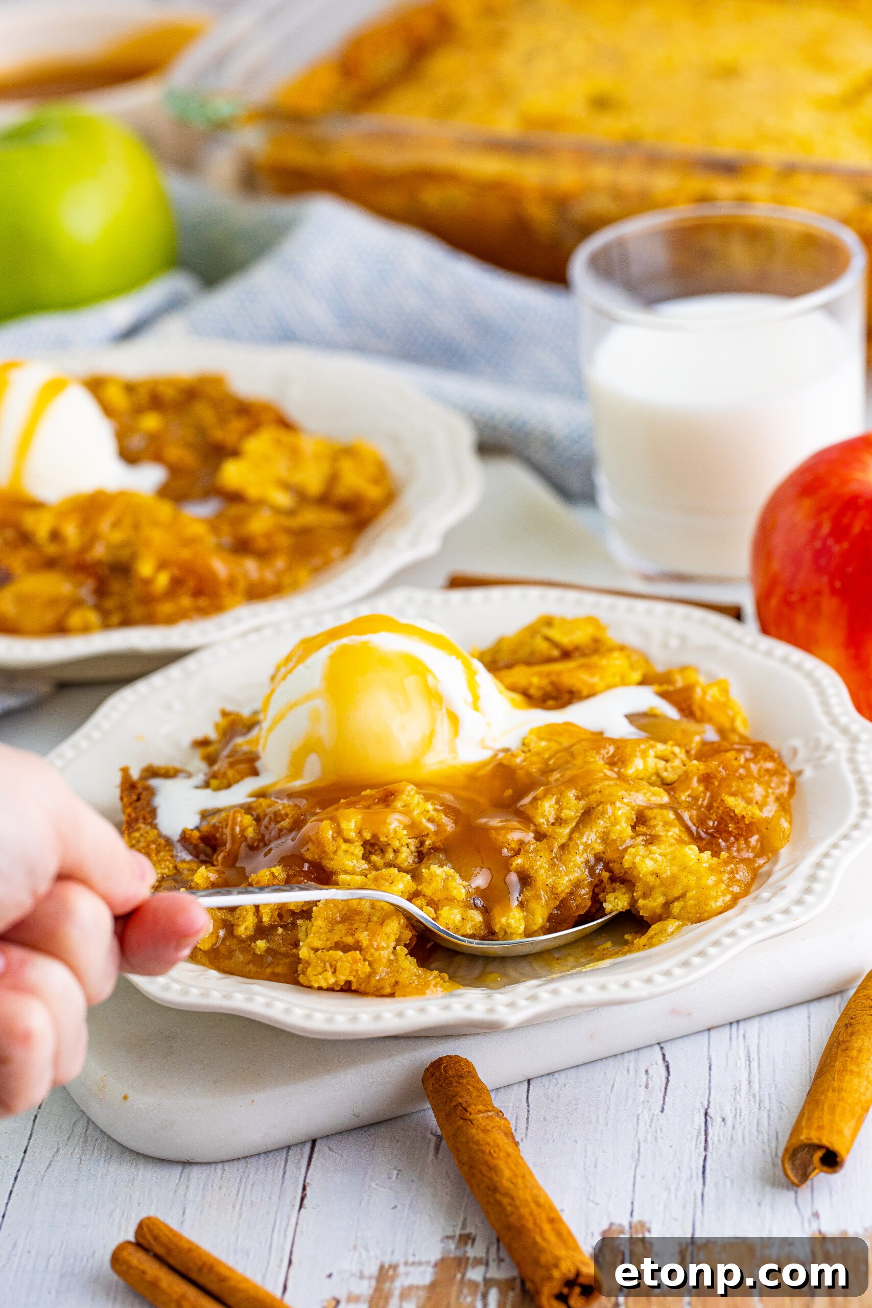 Close up shot of a spoon removing a bite of caramel apple dump cake from a white plate.